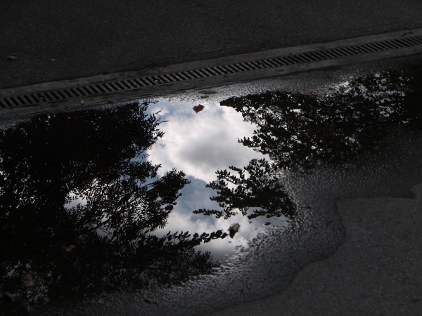 ciel se reflétant dans une petite flaque sur du goudron