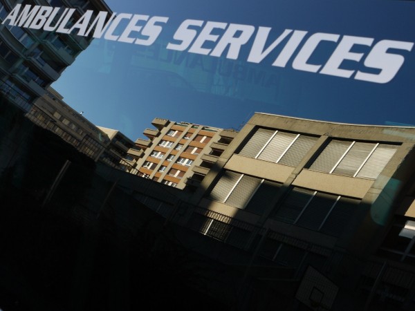 reflet d'immeuble au soleil dans la vitre d'une ambulance, avec les mots "ambulances services" sur la vitre