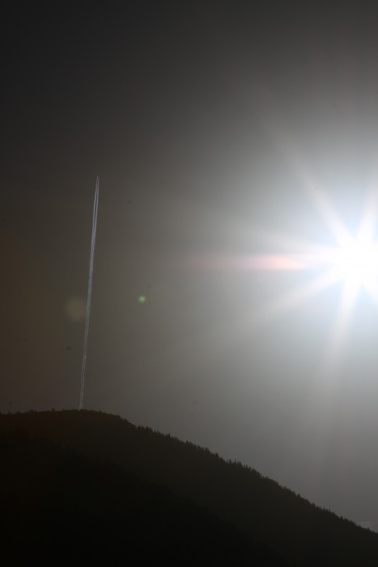 montagne en contre-jour avec soleil à droite de l'image et trace d'avion dans le ciel